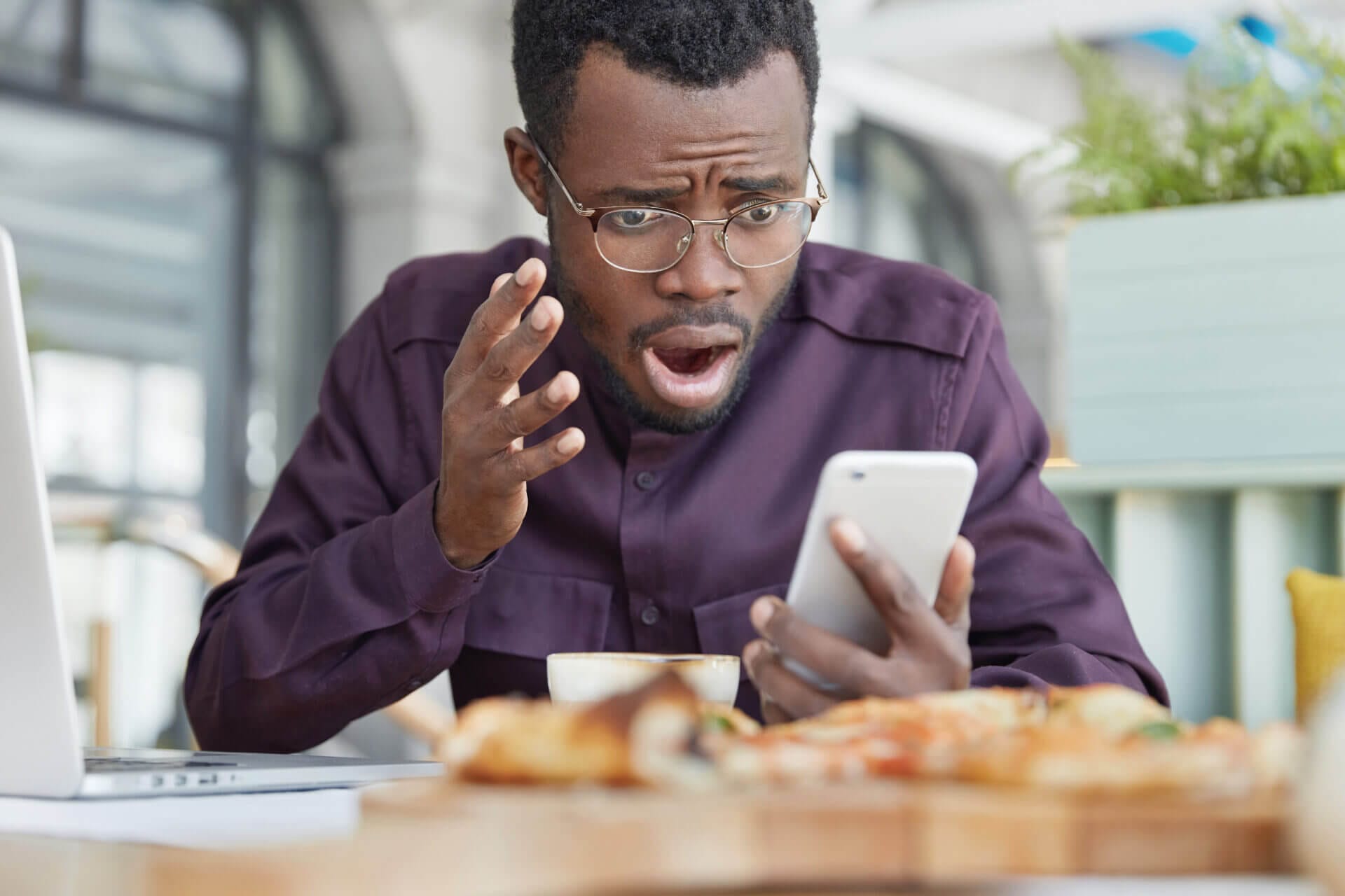 frustrated dark skinned male looks desperately into screen reads information smart phone sits coffee shop